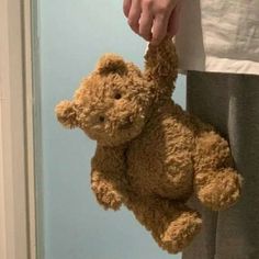 a person holding a brown teddy bear in their hand while standing next to a door