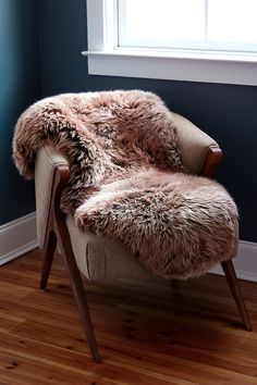 a chair with a fur on it in front of a window and wooden flooring