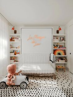 a child's room with a white crib and pink teddy bear on the floor