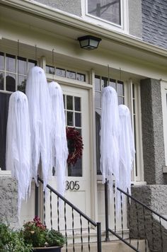 three white ghost decorations hanging on the front door of a house with black railings