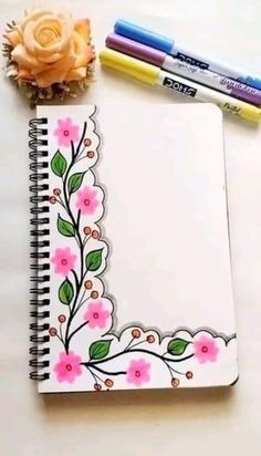 an open notebook with flowers and two crayons next to it