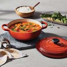 a red pot filled with food next to other dishes and utensils on a table