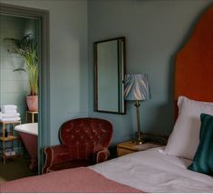 a bedroom with a bed, chair and mirror in it's corner next to a bathtub