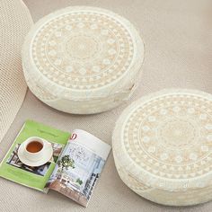 two round pillows and a cup of tea on the floor next to each other with an open magazine in front of them