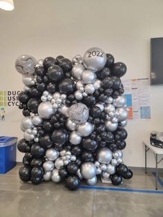 a bunch of black and silver balloons are stacked on top of each other in the middle of a room