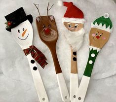 four wooden spoons decorated to look like santa claus, snowman and reindeer faces