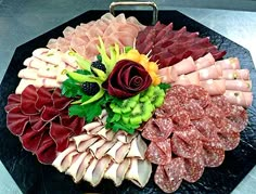 an assortment of meats and vegetables on a black platter with a rose in the center