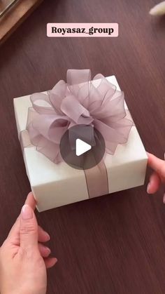 a person opening a white gift box with a pink flower on the front and side