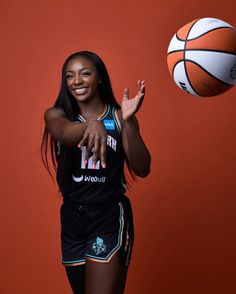 a woman is posing with a basketball in front of an orange wall and red background