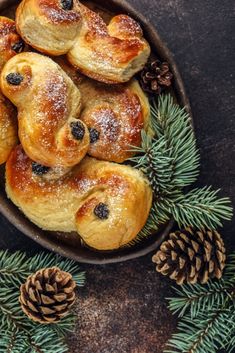 small pastries with blueberries and pine cones in a bowl surrounded by evergreen branches