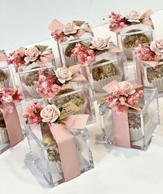 there are many small clear boxes with pink flowers in them and ribbons on the sides