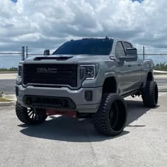 a silver truck parked in a parking lot next to a chain link fence and blue sky with clouds