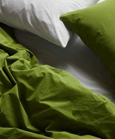 an unmade bed with green sheets and white pillow cases on top of each other