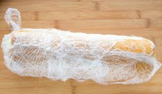 a loaf of bread wrapped in plastic sitting on top of a wooden cutting board