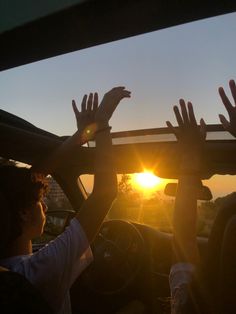 the sun is setting behind two people driving in a car with their hands on the roof