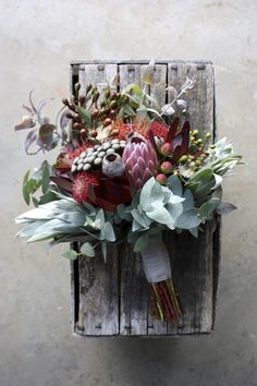 a bunch of flowers sitting on top of a wooden box with leaves and other plants