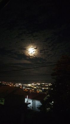 the full moon is shining brightly in the night sky over some houses and water with power lines running through it