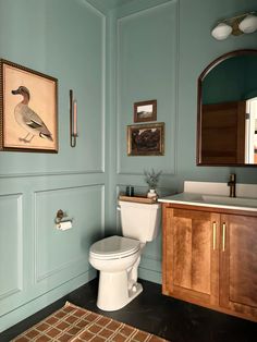 a bathroom with a toilet, sink and framed pictures on the wall above it's mirror