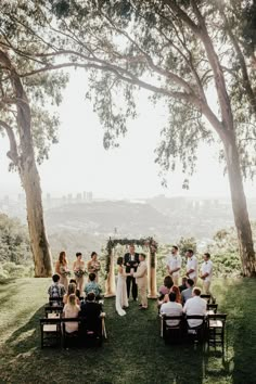 a group of people that are standing in the grass near some trees with chairs around them