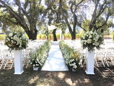 an outdoor ceremony setup with white flowers and greenery on the aisle, surrounded by trees