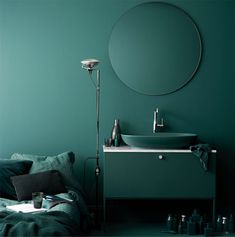 a bedroom with green walls and a round mirror on the wall above the bed is a sink