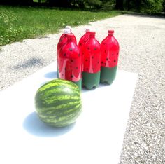 three watermelon and two plastic bottles sitting on the ground