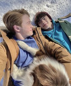 two people laying in the snow with a dog