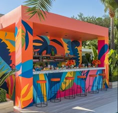 an outdoor bar with colorful painted walls and stools at the bar, surrounded by palm trees