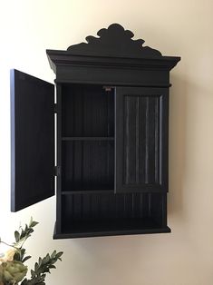 a black wooden cabinet sitting on top of a wall next to a potted plant