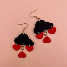 two pairs of red and black heart shaped earrings with dangling hooks on a pink background