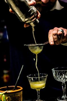 a bartender pours a cocktail into two glasses