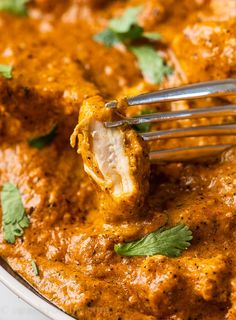 a fork is lifting up some food from a pan with sauce and cilantro