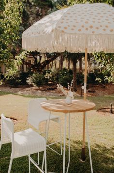 an umbrella and two chairs in the grass near a table with a cup on it