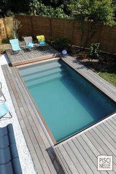 an empty swimming pool in the middle of a backyard with decking and lawn chairs