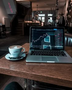 a laptop computer sitting on top of a wooden table next to a cup of coffee