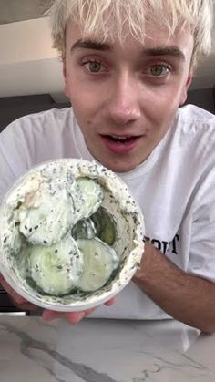 a young man is holding up a bowl with cucumbers in it and looking at the camera