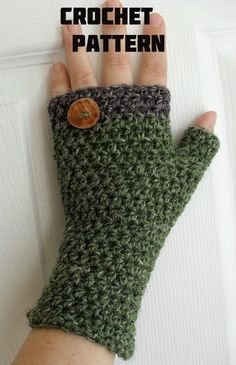 a hand is holding up a green crocheted mitt with a button on it