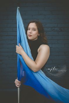 a woman holding onto a blue scarf in front of a brick wall with her hands on the pole