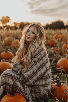 a woman sitting in the middle of a field with pumpkins on the ground and looking at the camera