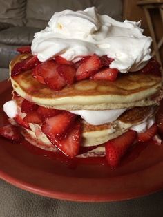 a stack of pancakes covered in whipped cream and strawberries