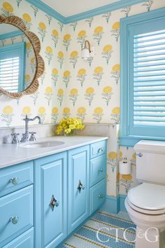 a bathroom with blue cabinets and yellow flowers on the wall next to the white toilet