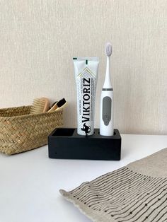 two toothbrushes and one tube of toothpaste on a table next to a basket