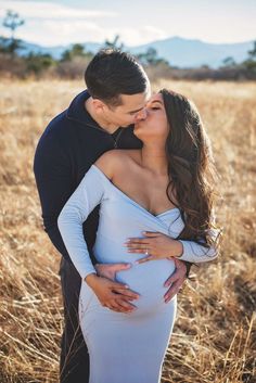 a pregnant couple cuddles and kisses in a field