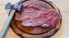 a piece of raw meat on a wooden plate with an old style hammer sticking out of it