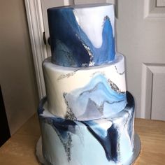 a three tiered cake with blue and white icing on the top, sitting on a wooden table