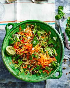 a green bowl filled with salad next to a fork and knife on top of a table