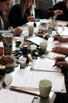 a group of people sitting around a table with papers and cups on it, writing