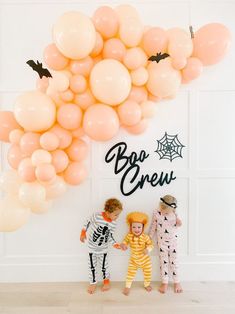 three children dressed up in halloween costumes standing next to a balloon arch with boo crew written on it