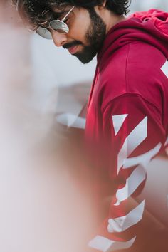 a man in a red hoodie looking down at his cell phone while wearing glasses