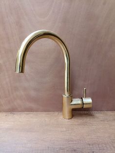 a gold faucet on top of a wooden table next to a pink wall